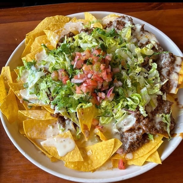 A large plate of nachos with ground beef, melted cheese, shredded lettuce, and pico de gallo.