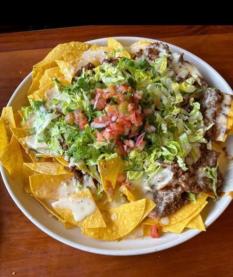 A large plate of nachos with ground beef, melted cheese, shredded lettuce, and pico de gallo.